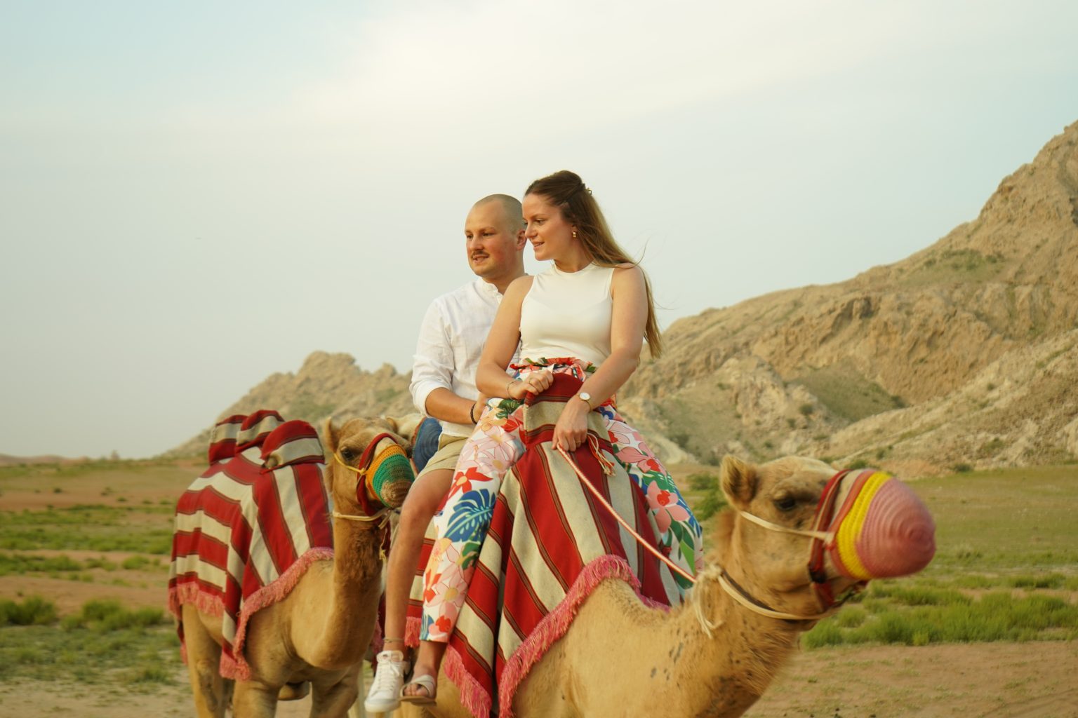 Couple enjoying camel trekking Dubai during a peaceful desert ride with scenic mountains in the background